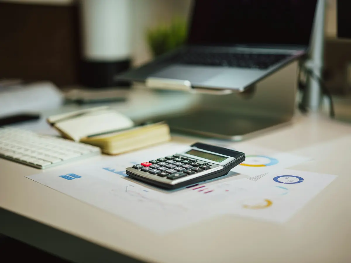 A desk with a laptop, calculator and financial reports
